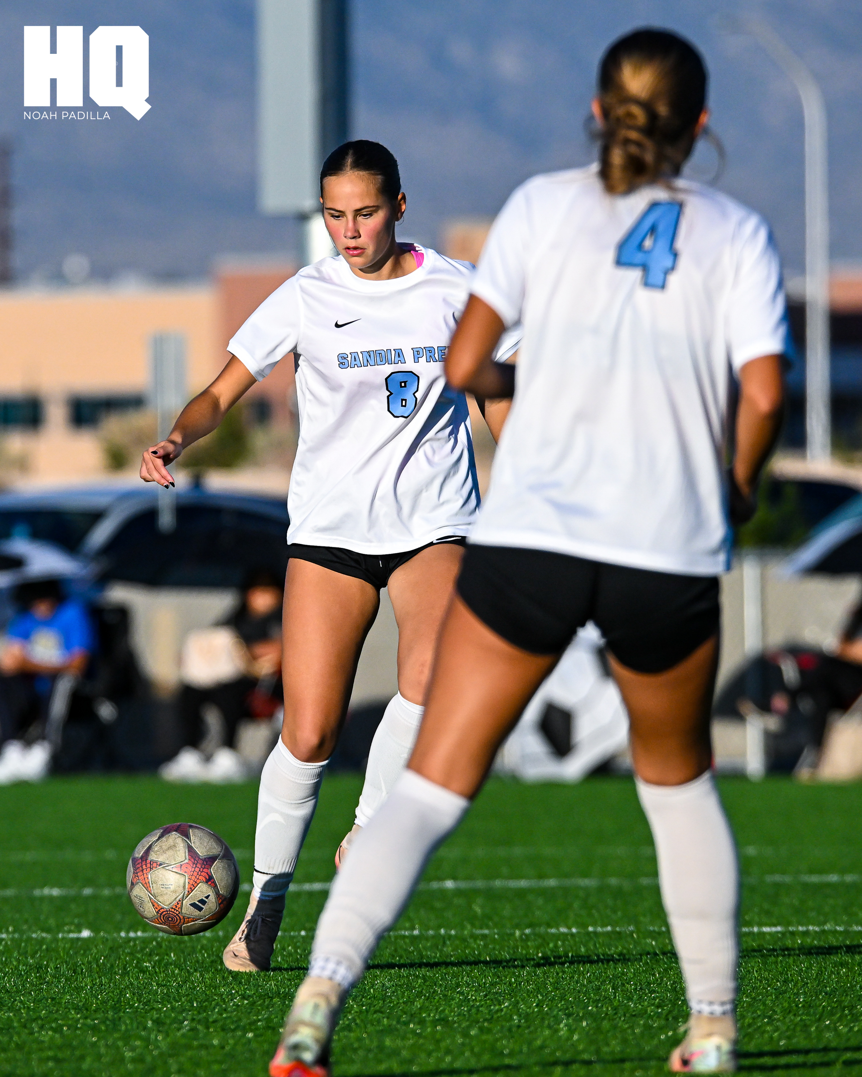 A Sandia Prep midfielder, Camryn McWilliams, wearing jersey number 8 prepares to pass the ball while her teammate, number 4 Maddie Dopson, stands in position ahead of her on the field.