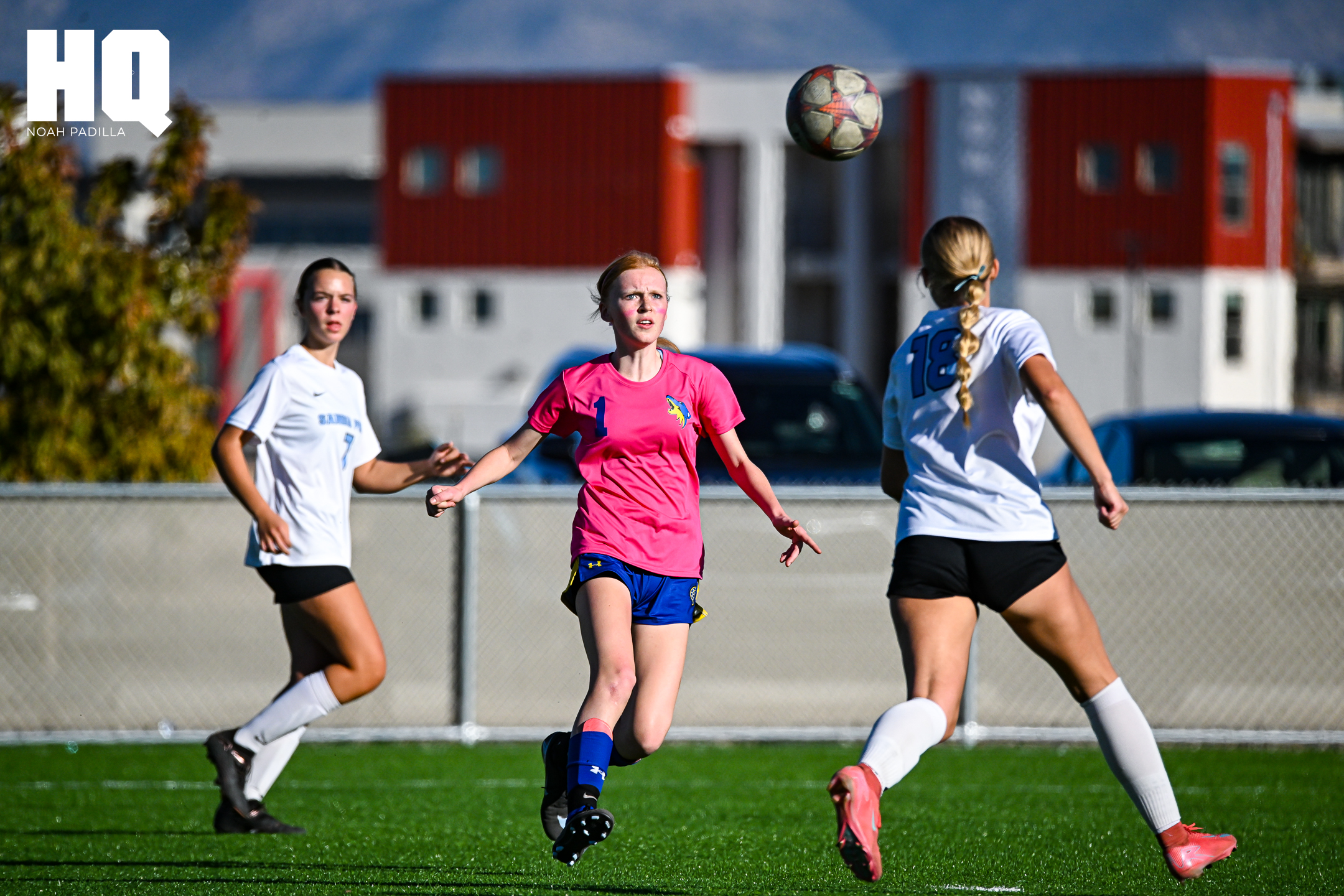 Lyla Patterson of Cottonwood Classical girls soccer wearing number 1 watches the ball in mid-air as two Sandia Prep defenders in white — one with number 18 — prepare to contest the play near the goal.